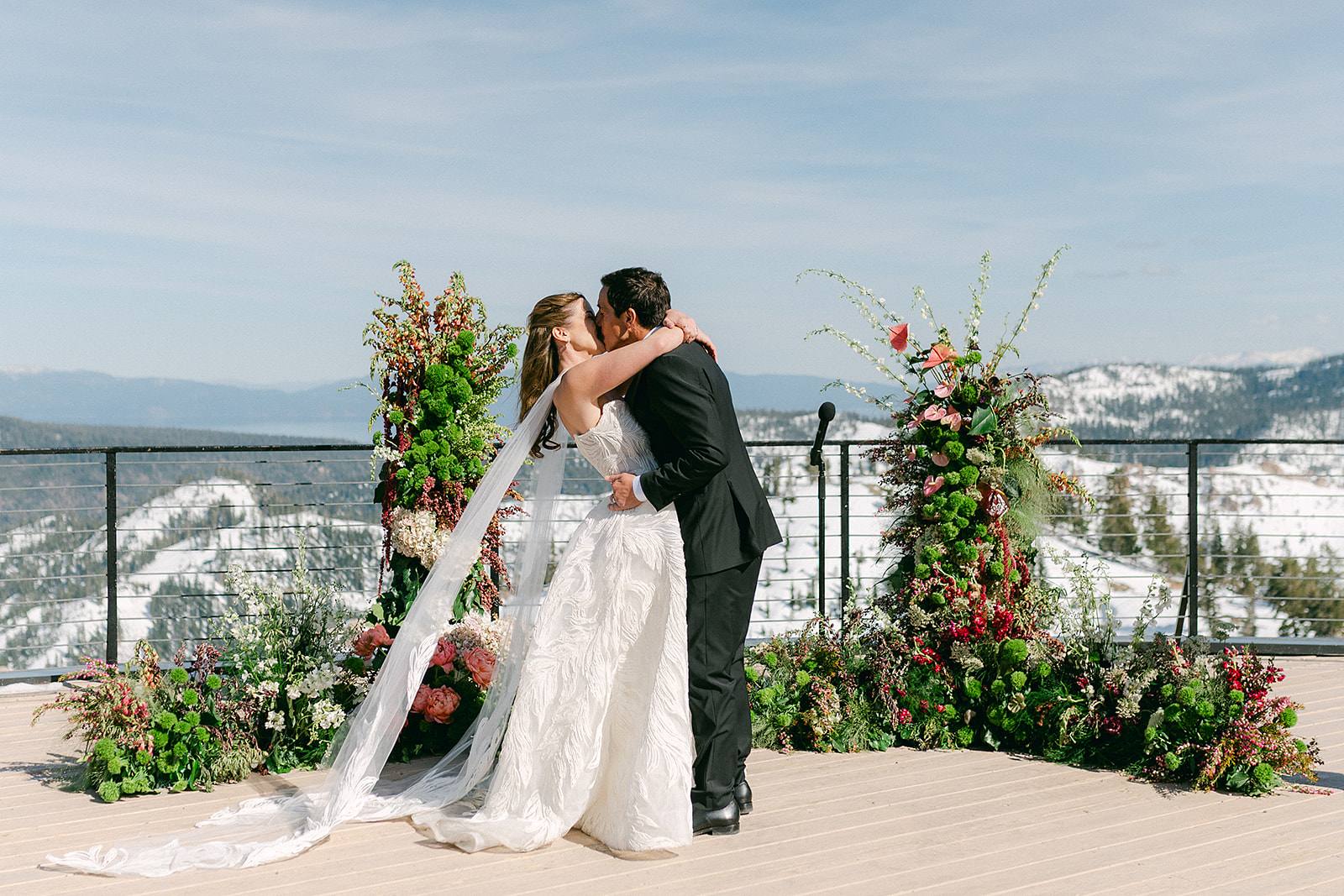Snowy Sierra mountaintop wedding ceremony: couple kissing between two towering floral installations